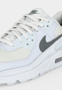Λευκό παπούτσι Nike Air Max με γκρι σήμα (swoosh), πάνελ από πλέγμα και δέρμα, λευκές κορδόνια και ορατή μονάδα αέρα στη σόλα.