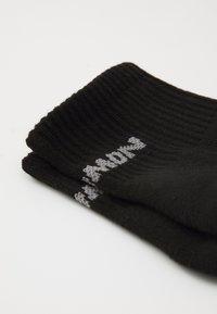 Calcetines negros con textura acanalada y texto bordado en gris a lo largo del borde superior. El material parece suave con una textura lisa y forma de calcetín estándar.