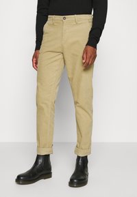 Beige manchesterbyxor med smal passform, med knappstängning, fickor och uppvikta muddar, kombinerade med svarta ankelboots.