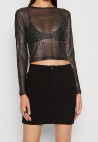 Svart långärmad mesh-topp med metallisk prickdesign, kombinerad med en svart denimkjol med framfickor och en figursydd silhuett.