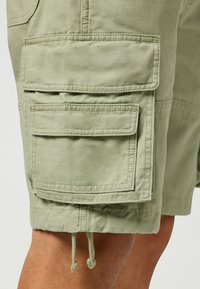 Olivgrüne Cargo-Shorts aus strapazierfähigem Material, ausgestattet mit mehreren Klappentaschen und einem verstellbaren Kordelzugsaum.