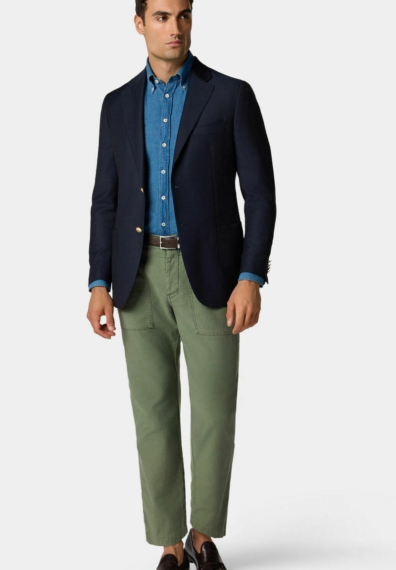 Námořnický blazer, světle modrá denimová košile, zelené kalhoty, hnědý opasek a tmavé boty. Blazer má zlaté knoflíky; kalhoty mají viditelné kapsy.