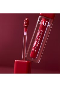 Rouge à lèvres liquide mat dans un tube transparent avec un capuchon rouge. L'applicateur montre une teinte rouge riche ; le texte sur le tube indique la marque et le nom du produit.