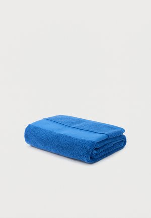 Folded blue terry cloth towel with a textured band, placed on a white surface.