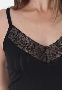 Black camisole with lace trim on a V-neckline. Features thin straps and ribbed texture throughout the fabric. Subtle lace floral pattern.