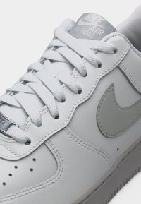 Primo piano di una sneaker Nike Air bianca che mostra i lacci testurizzati, pannelli in pelle cuciti, perforazioni e il logo Nike swoosh grigio sul lato.