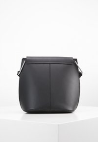 Černá kožená kabelka zaobleného tvaru, ploché zavírání a stříbrné kovové prvky. Hladká textura s minimalistickým designem.