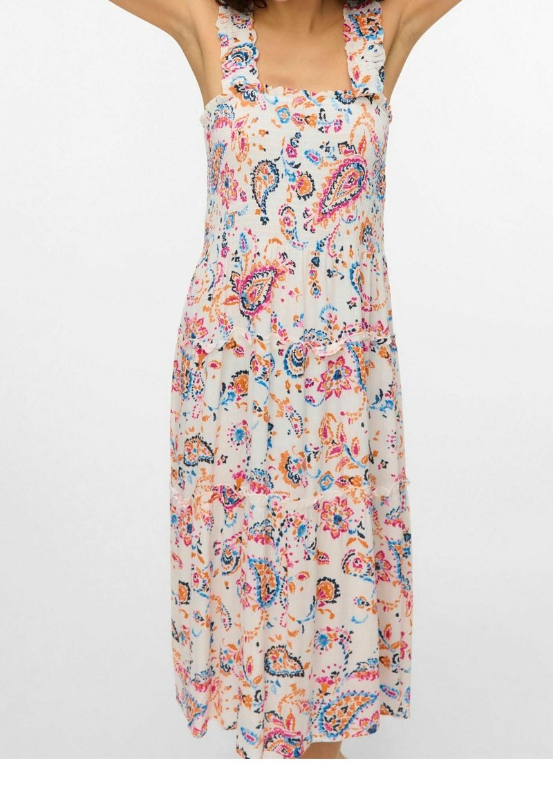 Femme portant une robe blanche sans manches avec des motifs cachemire et floraux multicolores en rose, bleu et orange.