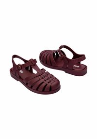 Sandali in plastica modellata color bordeaux con design intrecciato, schienale aperto e cinturino alla caviglia regolabile. Sottopiede testurizzato e suola in gomma solida.