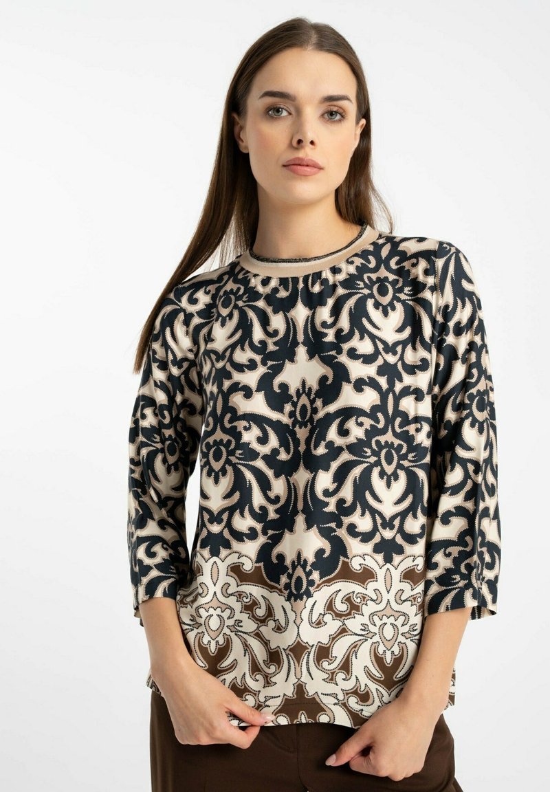 Bluzka z długim rękawem w kolorze kremowym, zdobiona skomplikowanymi wzorami kwiatowymi w odcieniach granatu i brązu. Okrągły dekolt, wykonana z miękkiego materiału o gładkiej fakturze.