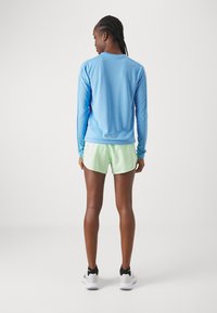 Langermet, lys blå treningsskjorte sammen med mintgrønne shorts. Har glatt stoff, tettsittende design og svarte løpesko.