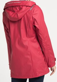 Czerwona wodoodporna kurtka z kapturem, o gładkiej fakturze, skośnym kroju i odblaskowym akcentem na ramieniu. Wyświetlony widok z tyłu.