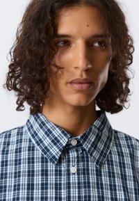 Geruit overhemd met marineblauw, lichtblauw en witte patronen. Knopen-kraag, korte mouwen en een gladde katoenachtige textuur.