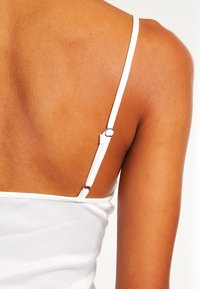 Gros plan sur le haut du dos et l'épaule d'une personne portant un haut blanc sans manches avec une bretelle réglable et une peau lisse.