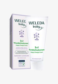 Biała plastikowa tubka z zielonym napisem i fioletowymi kwiatowymi akcentami, opisana jako "WELEDA baby 3in1 Wundschutzcreme." Towarzyszy jej pasujące pudełko.