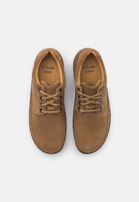 Chaussures à lacets en daim brun avec un bout arrondi, une doublure beige et des coutures contrastées. Elles possèdent des lacets épais et des semelles en caoutchouc.