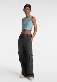 Top corto azzurro chiaro con scollo rotondo, abbinato a pantaloni cargo neri con più tasche e un taglio oversize. Footwear beige.
