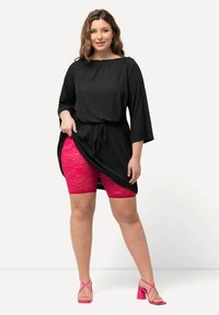 Zwarte, gestructureerde top met driekwartmouwen en een strik taille, gecombineerd met felroze kanten fietsshorts en bijpassende hoge hakken.