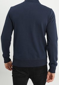 Felpa blu navy con una texture a coste, maniche lunghe e un bordo elastico. Presenta un colletto alla cinese e dettagli minimi.