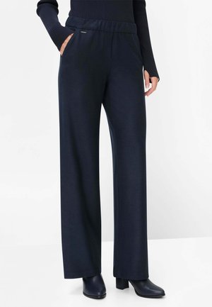 Woman wearing navy wide-leg pants with elastic waistband, hands in pockets, paired with black heeled ankle boots and a black ribbed top.