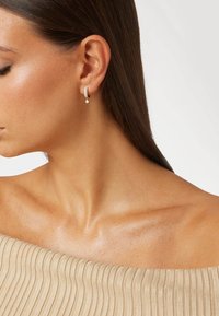 Orecchini a cerchio in argento con diamanti, caratterizzati da un design a goccia con un accento in cristallo a forma di pera. Texture liscia e lucida.