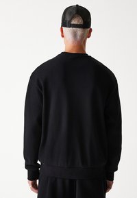 Schwarzer gerippter Sweatshirt mit lockerer Passform, rundem Ausschnitt und elastischem Bund, von hinten mit strukturierter Oberfläche dargestellt.