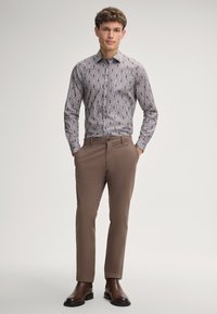 Overhemd met knopen in een ingewikkeld bruin en wit bloemenpatroon, gecombineerd met een slim-fit bruine broek en donkere leren boots.