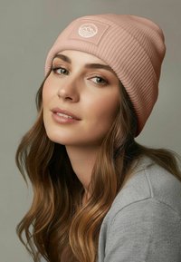Pink ribbed beanie featuring a front patch with a wave and mountain graphic. Thick texture, snug fit, and soft fabric.
