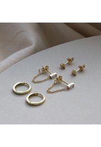 Goldene Creolen und herzförmige Steckerohrringe mit einer Kettendetails. Glatte und glänzende Oberfläche. Herzakzente an den Steckern.