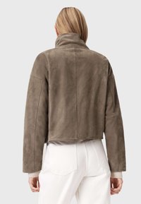 Zkrácená hnědá semišová bunda s vysokým límcem a uvolněným střihem, s hladkou texturou a dlouhými rukávy, doplněná o bílé kalhoty.