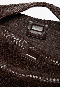 Brun vævet håndtaske med en karakteristisk fletstruktur, der har mørke lædermærker prægede med "Massimo Dutti." Kanterne er bølgede.