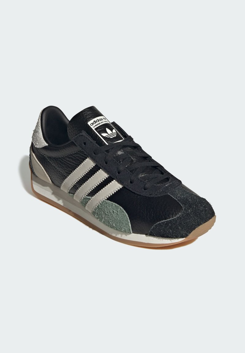 Czarny sneaker z fakturowanej skóry i zamszowymi akcentami. Ma trzy białe paski, gumową podeszwę oraz etykietę z logo na języku.