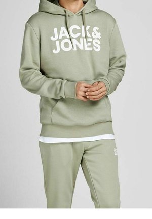 Homme portant un sweat à capuche vert clair et un pantalon de survêtement assorti avec l'inscription "JACK & JONES" en blanc sur le devant du sweat à capuche et la cuisse du pantalon.