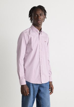 Camicia a righe rosse e bianche con colletto, maniche lunghe e un piccolo logo sul petto; abbinata a jeans di denim blu.
