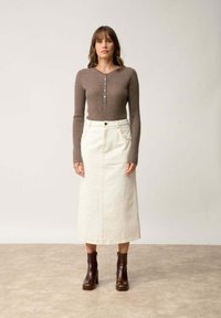 Brązowa, prążkowana bluzka z długim rękawem z guzikami, zestawiona z kremową, dżinsową spódnicą maxi oraz ciemnobrązowymi botkami na obcasie.