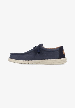 Scarpa slip-on in tela di colore blu navy con finitura testurizzata, dotata di una suola in gomma crema, cuciture sottili e un piccolo logo sul tallone.