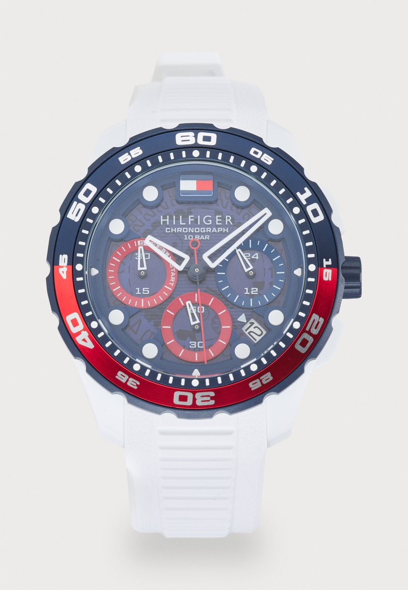 Tommy Hilfiger chronograph watch with white strap, blue and red bezel, three subdials, date display, and branded logo on the dial.