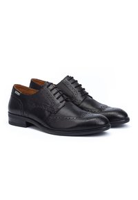 Le scarpe in pelle nera hanno un design classico con dettagli brogue, punta rotonda e un tacco basso impilato. Fodera interna marrone scuro.
