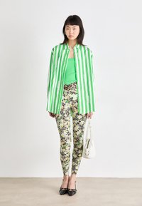Grønt og hvitt stripet oversized skjorte, lagdelt over en grønn topp, parret med mønstrede leggings med blomster- og leoparddesign.