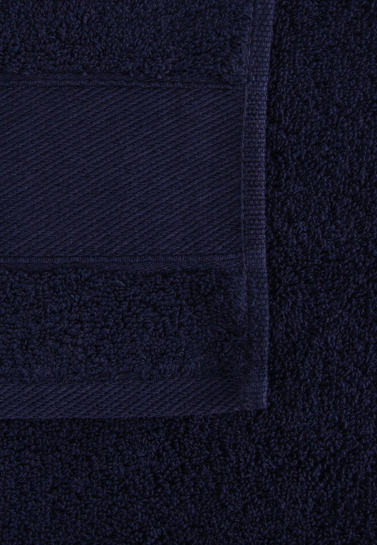 Serviette en coton bleu marine foncé avec un motif rayé texturé et lisse, pliée sur un fond de serviette assortie.