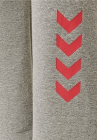 Ljust grå atletisk tyg har en vertikal kolumn med fyra röda chevronformer, vilket betonar en modern och sportig design.