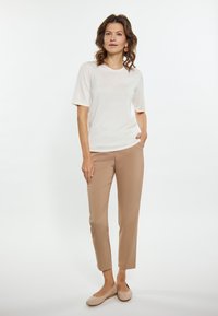 Let varierende T-shirt i let stof med korte ærmer, parret med beige slim-fit bukser og beige flade sko, sat mod en neutral baggrund.