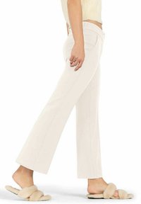Light beige flared trousers featuring a smooth texture, straight seams, and subtle pockets, paired with fluffy slide sandals.