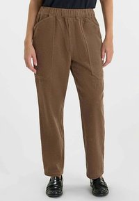 Bruine textuurbroek met een losse pasvorm, voorzien van een elastische tailleband en zijzakken. Gecombineerd met zwarte schoenen.