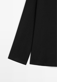 Zwarte longsleeve top met een gladde textuur, hoge halslijn en aansluitende manchetten. Materiaal lijkt zacht, met een nette zoom en geen zichtbare patronen.