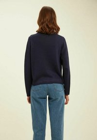 Pull en maille bleu marine à manches longues, encolure ronde et ourlet côtelé. Associé à un jean taille haute bleu clair.