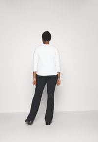 Witte top met driekwartmouwen gecombineerd met zwarte, rechte broek. Glad materiaal met een eenvoudig ontwerp, met een detail op de rug bij de nek.