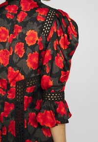 Schwarzes Blumenkleid mit großen roten Blumenmustern, puffärmeligen Ärmeln, Spitzenverzierungen und einem gerafften Saum. Glattes Material mit texturiertem Finish.