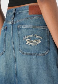 Denimskjørt i lys blå med et lærmerke i livet. Har en baklomme med hvit brodert tekst: "Authentic Original Tommy Jeans."