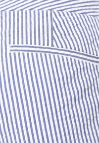 Pasek materiału w niebiesko-białe pasy o naprzemiennym układzie, z fakturą i widoczną kieszenią po lewej stronie.